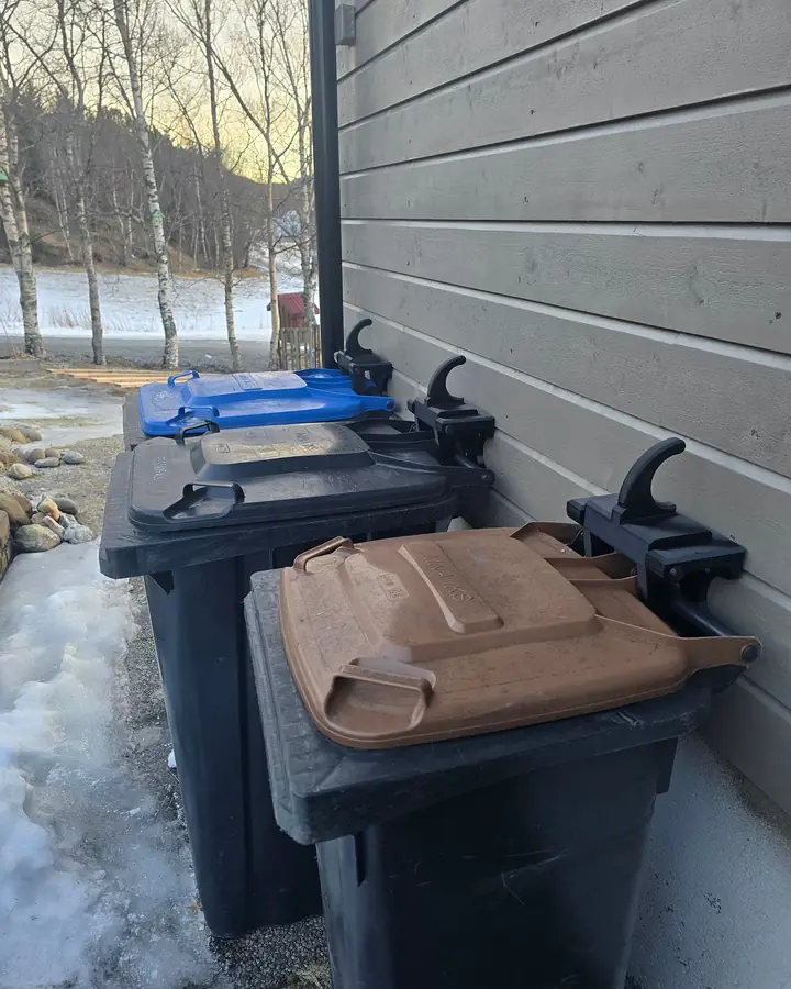 Tre søppeldunker festet til husvegg med printet veggfeste, vinterlandskap i bakgrunnen